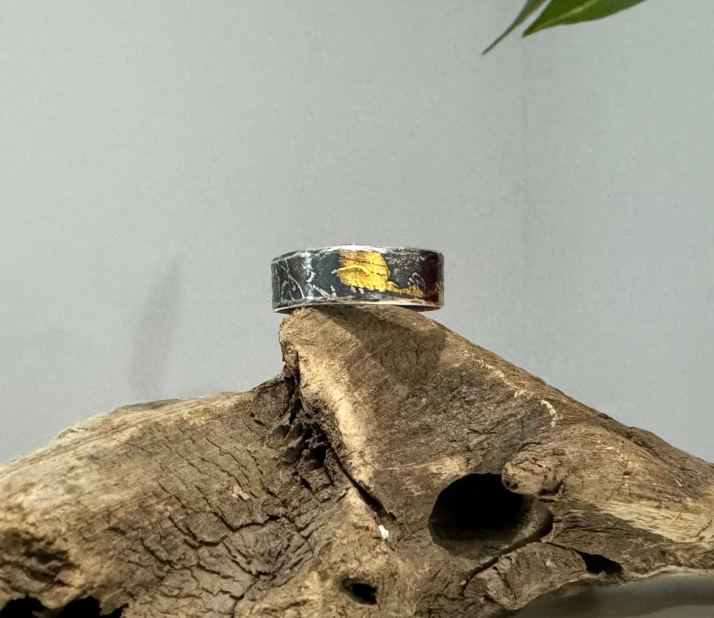 Silver ring with gold accents on a piece of driftwood against a gray background