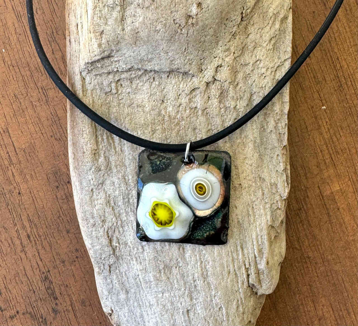 Handcrafted floral enamel necklace featuring a square pendant with white and yellow flower designs on a black background. One of a kind art jewelry.