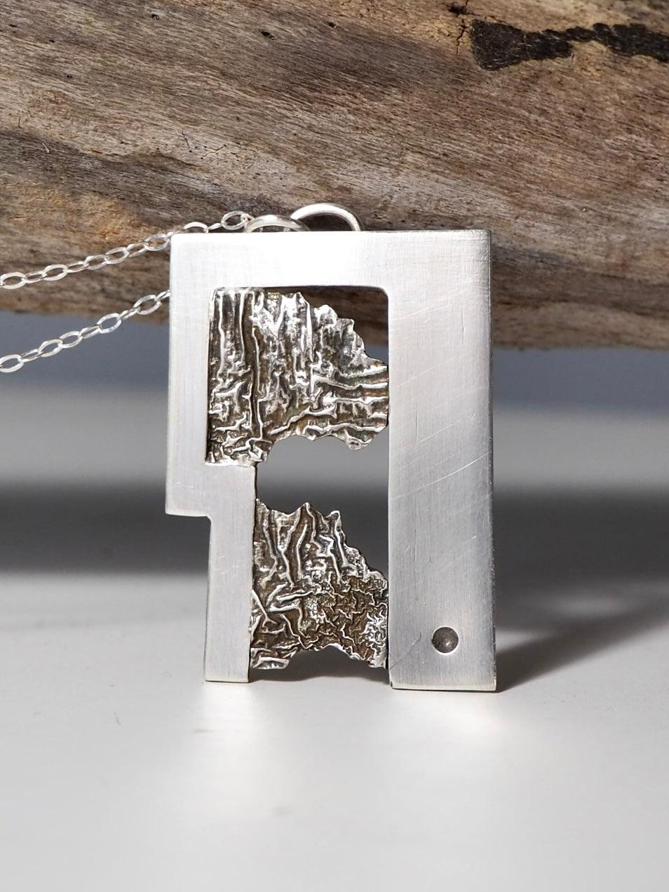 This image shows a unique, handcrafted pendant made of silver.  
Modern silver pendant with reticulated texture and geometric cut-out design.