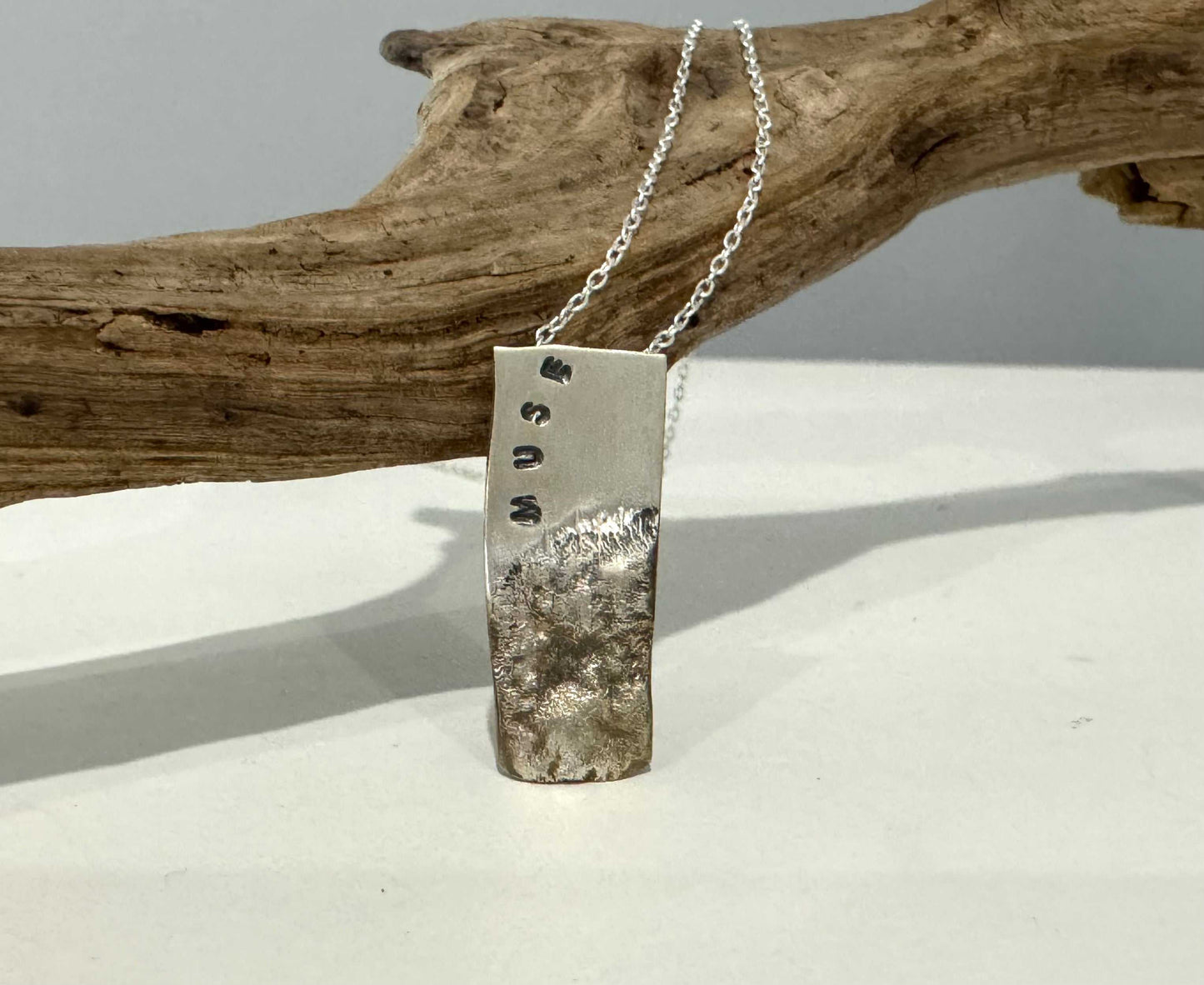 bumpy silver pendant with muse stamped on it