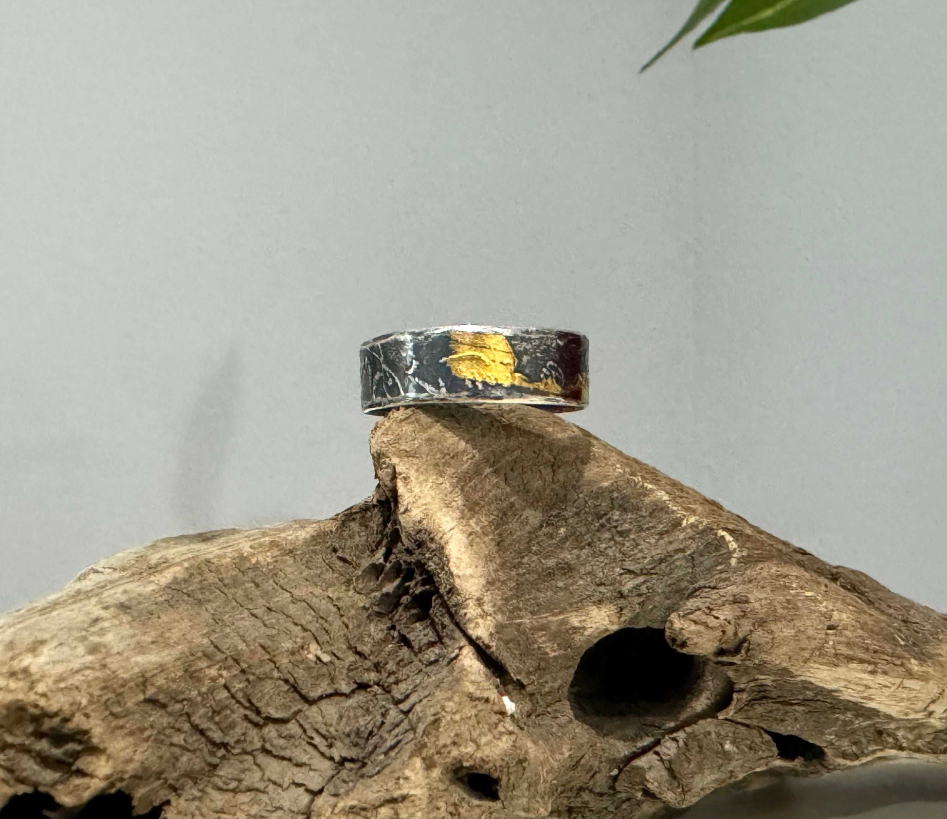 Silver ring with gold accents on a piece of driftwood against a gray background